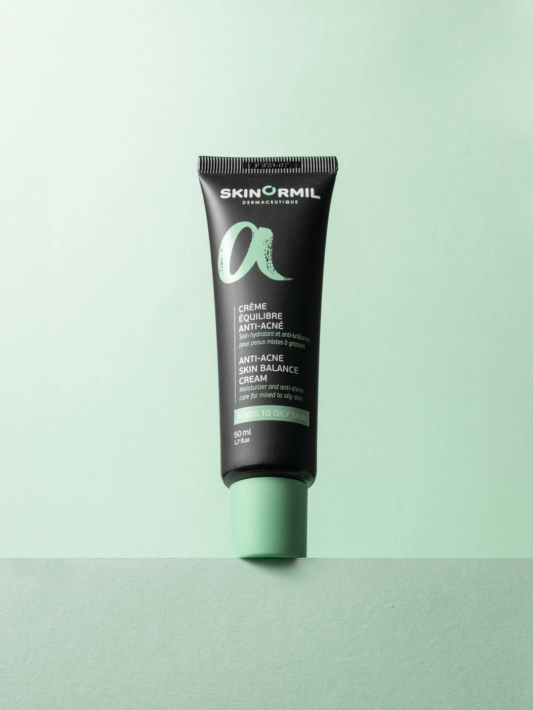 Крем Skinormil Anti-Acne Skin Balance Cream в черном тюбике с мятно-зеленой крышкой на нежно-зеленом фоне.